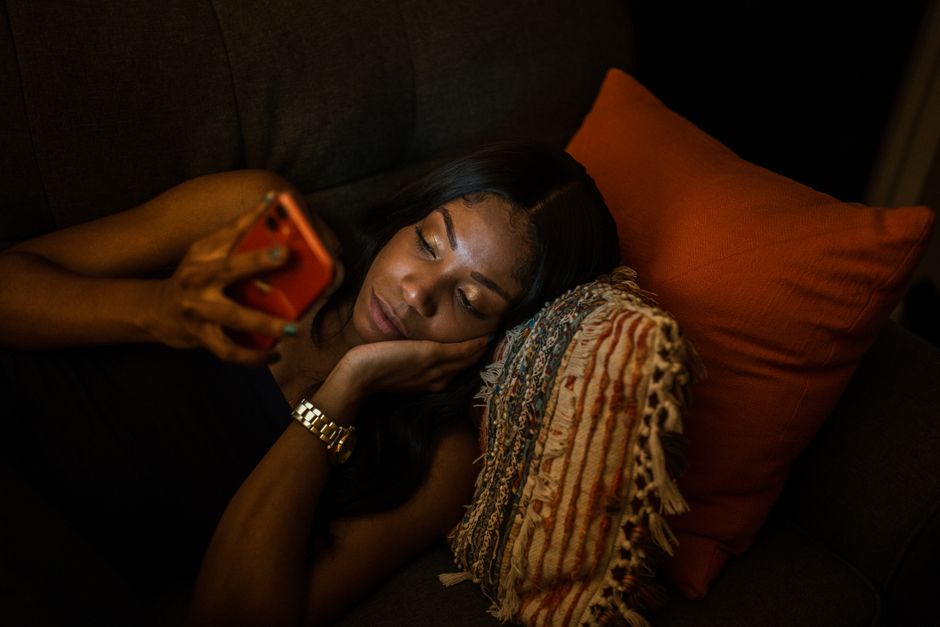 person watching television while using smartphone on couch